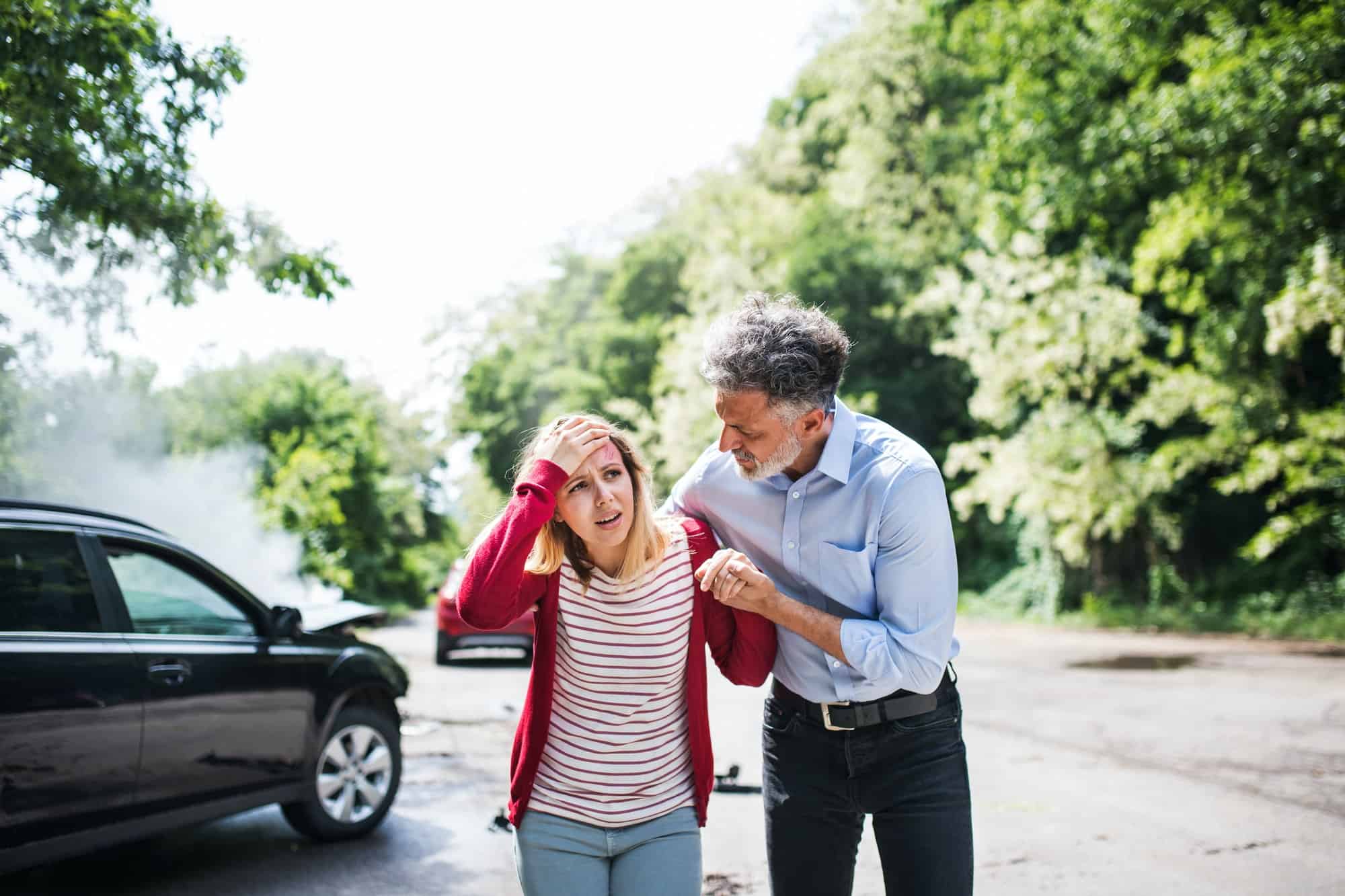 a mature man helping a young woman to walk after a car accident